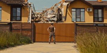 photo of man standing against destruction of a house
