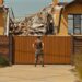 photo of man standing against destruction of a house