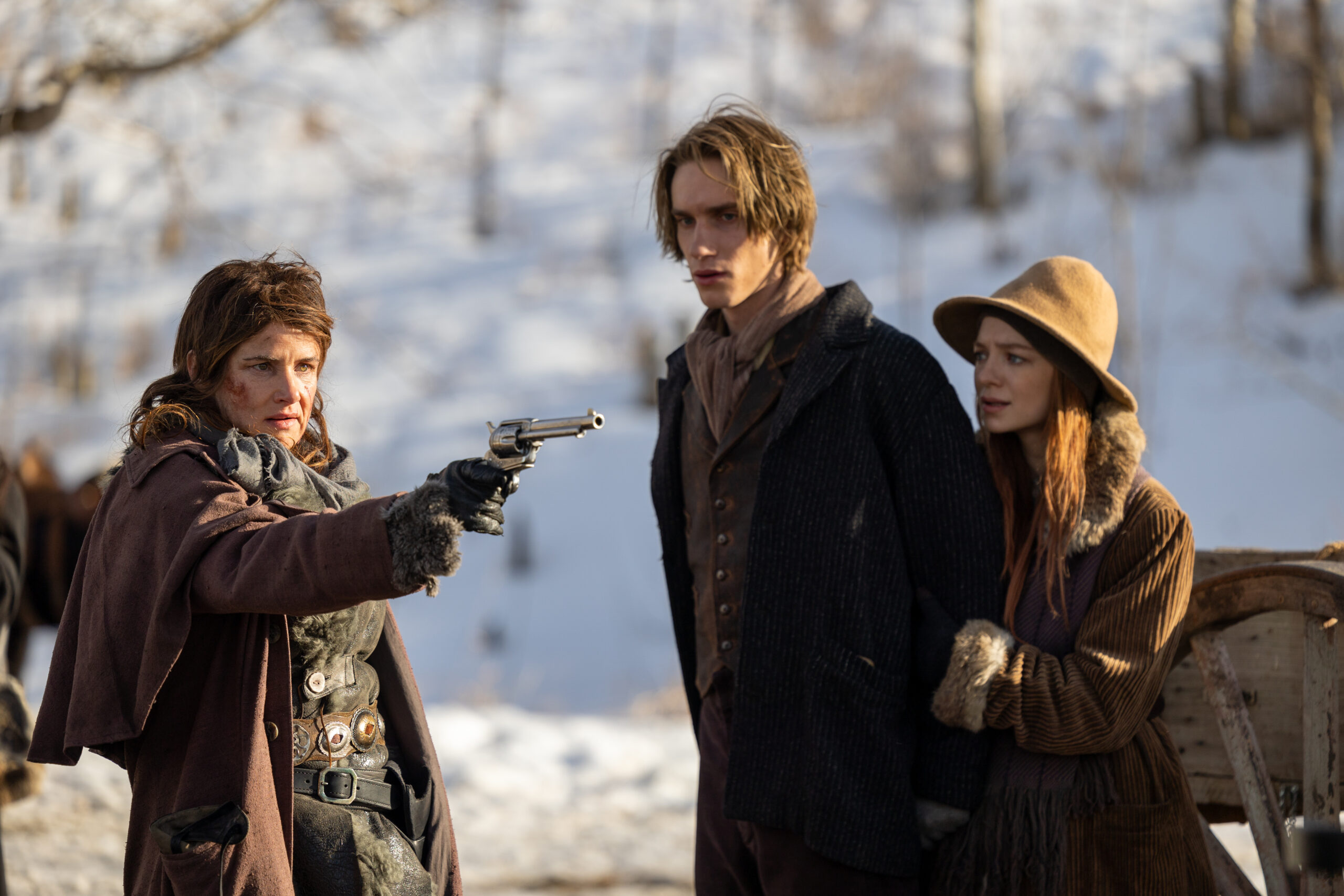 A feral looking woman points a gun at two 1800s teens