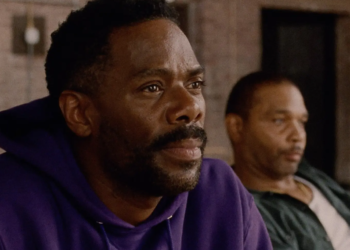a black man in a purple hoodie sits next to another black man