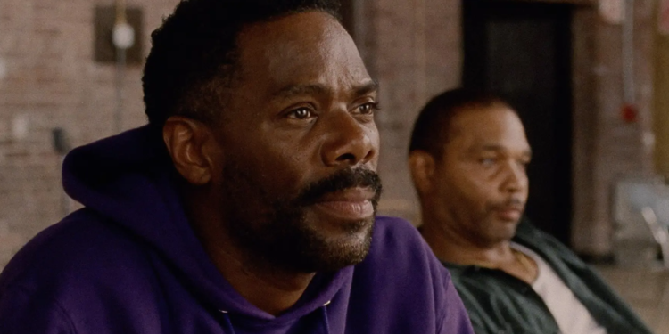 a black man in a purple hoodie sits next to another black man