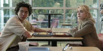 a young man and a young woman sit at a cafeteria table