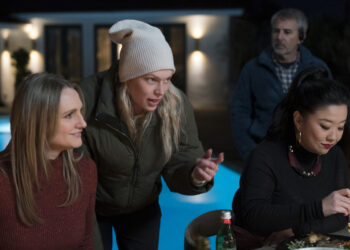a woman directing two actors on set by a pool