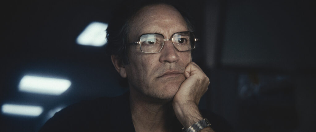 a man staring at a TV screen, with the screen reflected in his glasses