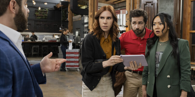 two women and a man hold an ipad and look shocked at another man