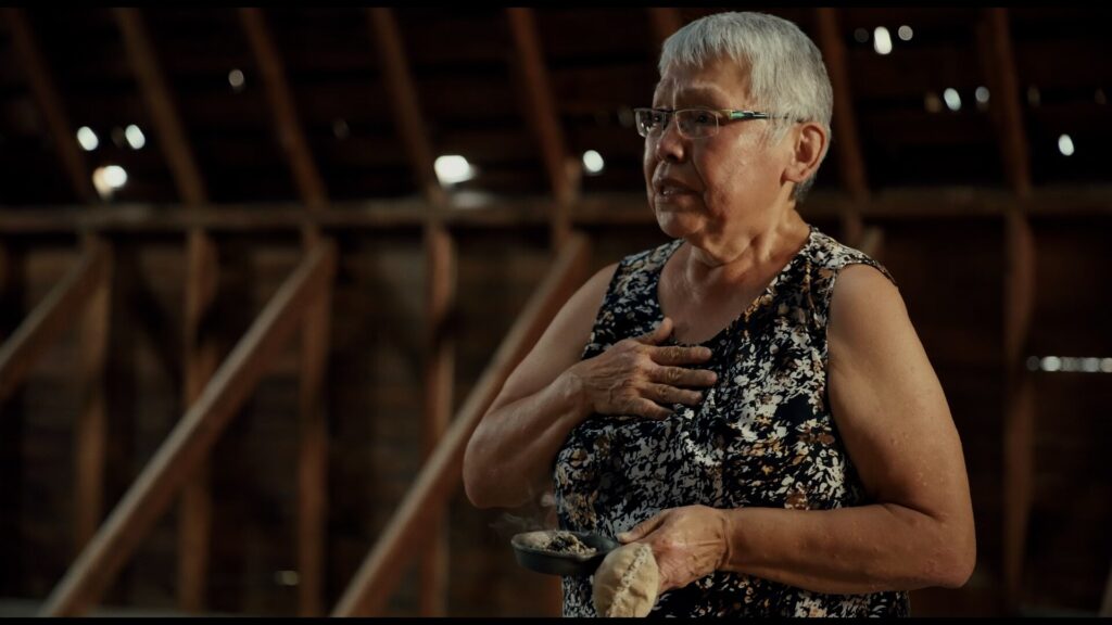 An older woman in an attic holding her hand to her chest