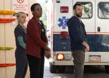 three people stand outside of an ambulance