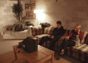 a man and a woman sit on a couch in front of a wall of cinder blocks