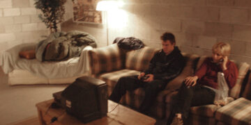 a man and a woman sit on a couch in front of a wall of cinder blocks