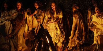 a group of teenage girls dance around a campfire at night