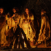a group of teenage girls dance around a campfire at night