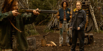 a teenager points a gun as two other teenagers watch in the wilderness