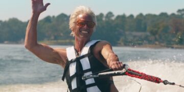 a naked man with white hair in a life preserver jet skiing