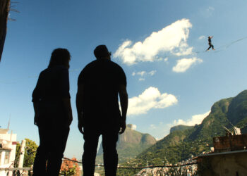 two men watch a man on a slackline