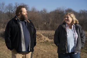 Iceland and Sam, a man and a woman, stand in a field in Kansas on Somebody Somewhere