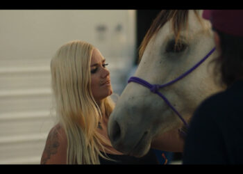 a blond girl looking at a horse