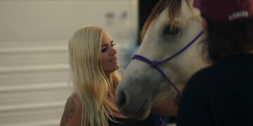 a blond girl looking at a horse