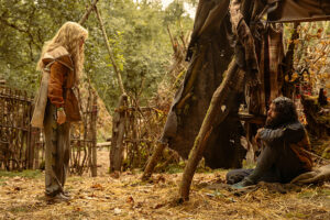 a girl stands in the woods over a hurt man