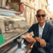 stanley tucci stands by a food stand in italy