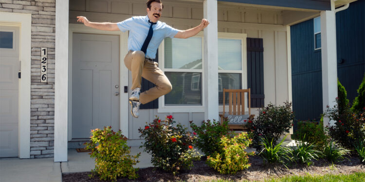 Ted lasso leaps in the air outside of a house